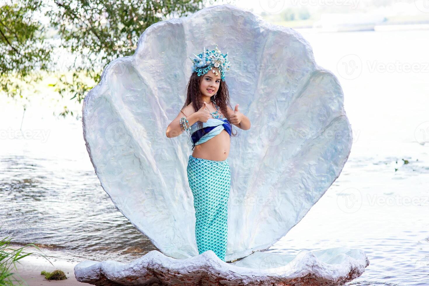 A cute girl in a mermaid costume stands outdoor in a large sea shell, photo
