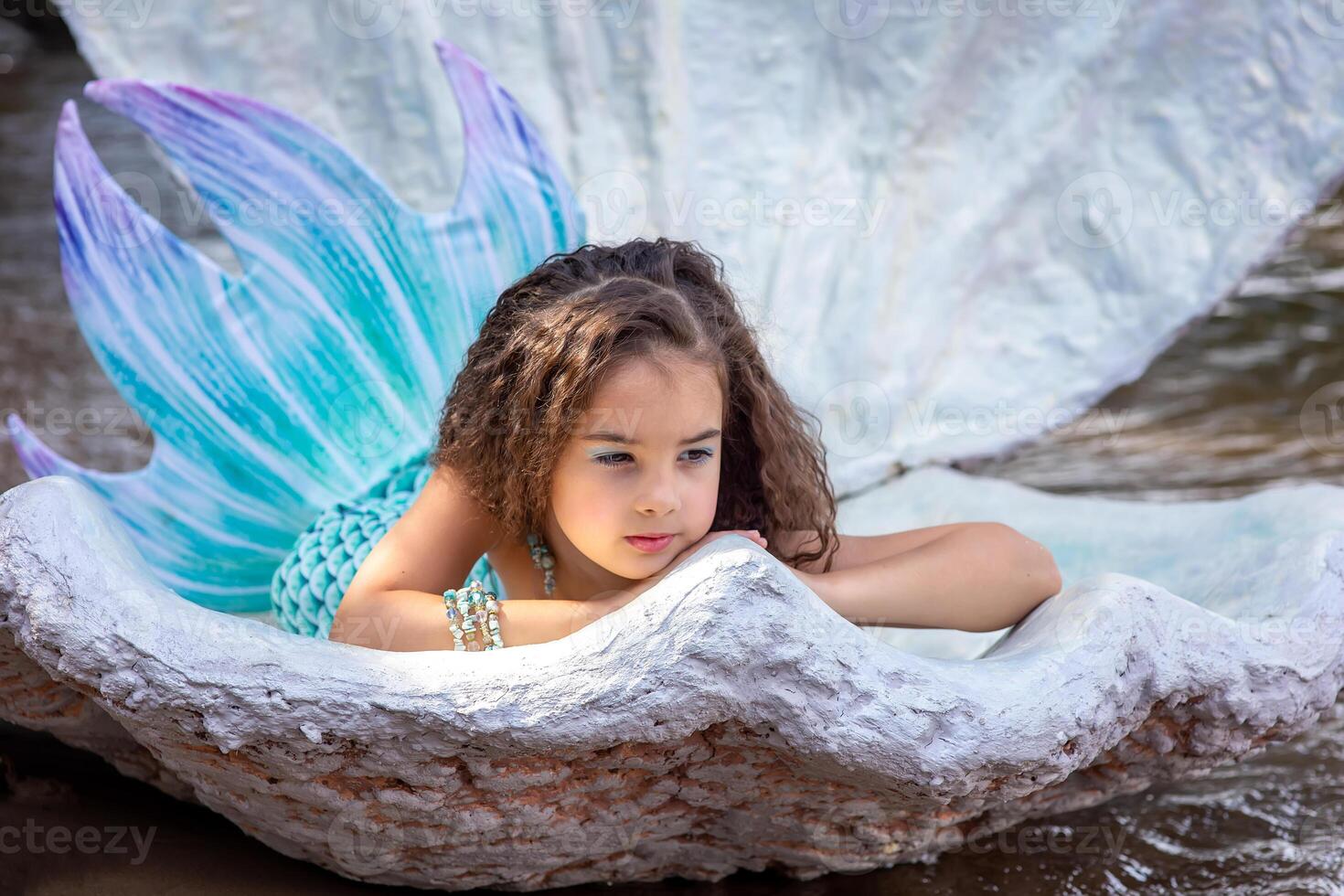 A beautiful girl in a turquoise mermaid costume in a large sea shell photo