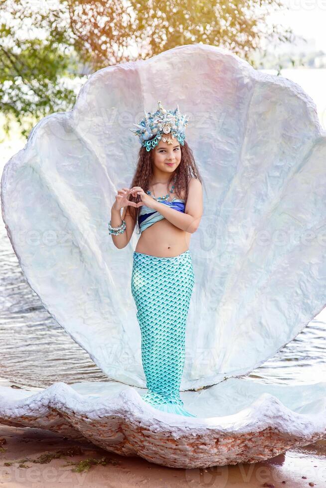 A little girl in a mermaid costume is standing outdoors, in a large seashell photo
