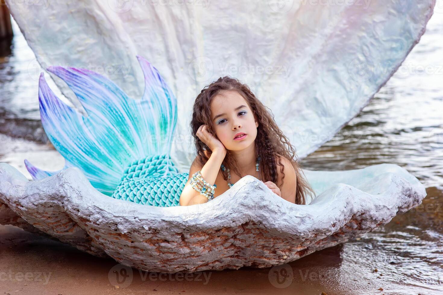 A pretty girl in a turquoise mermaid costume in a large sea shell photo