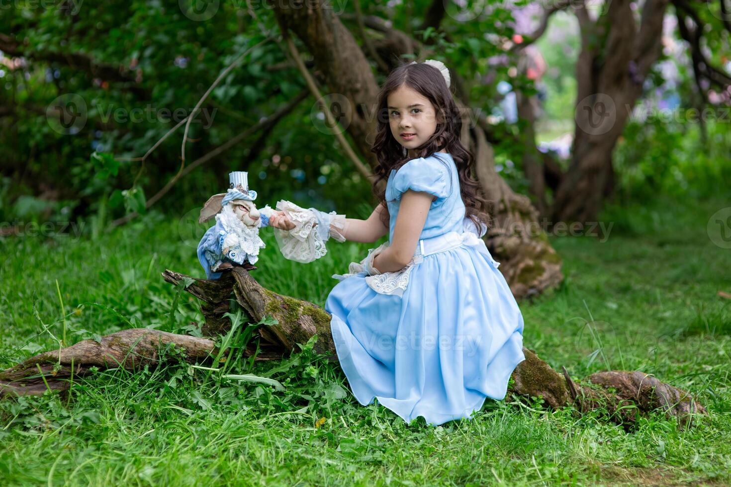Young caucasian girl in blue dress playing with stuffed rabbit in enchanted forest photo