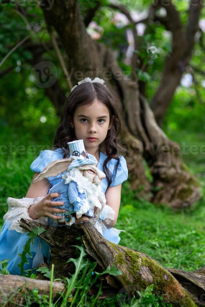 Young caucasian girl in blue dress holding doll in enchanted forest setting photo