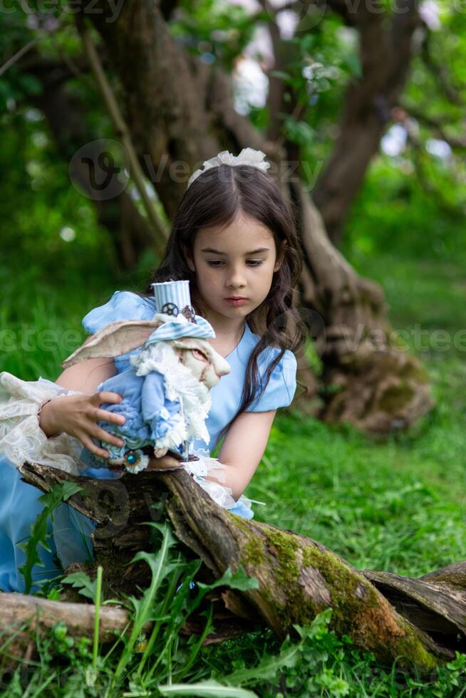 Young caucasian girl in blue dress with plush rabbit in green forest setting photo