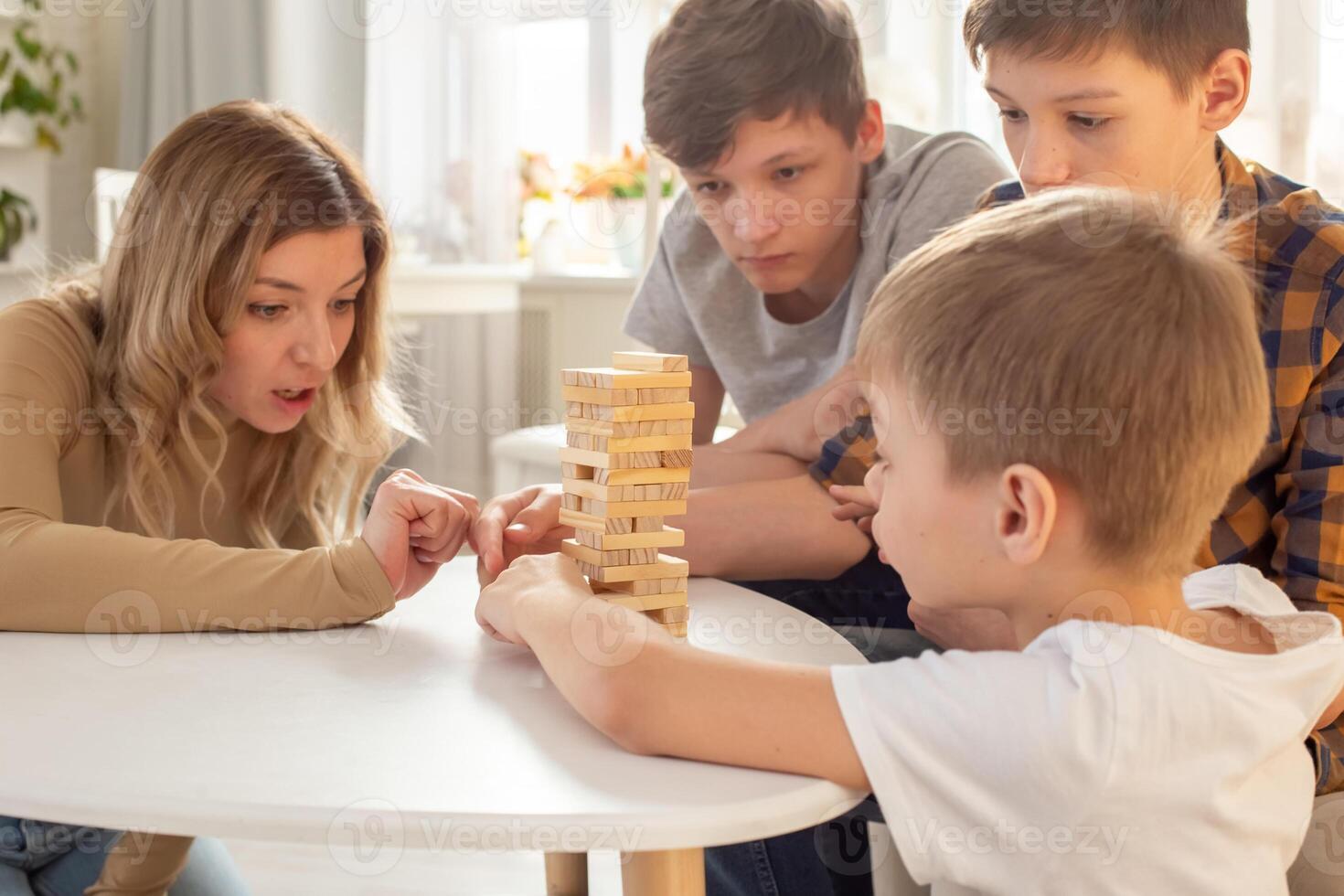 A cute mother and three sons are enthusiastically playing a board game made of wooden rectangular blocks photo