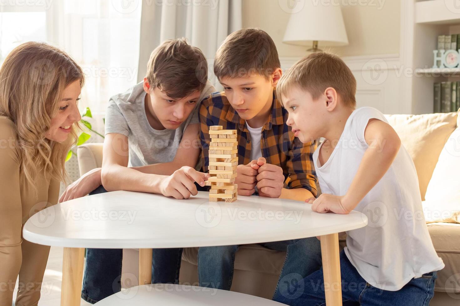 A smiling woman and three boys are enthusiastically playing a board game made of wooden rectangular blocks photo