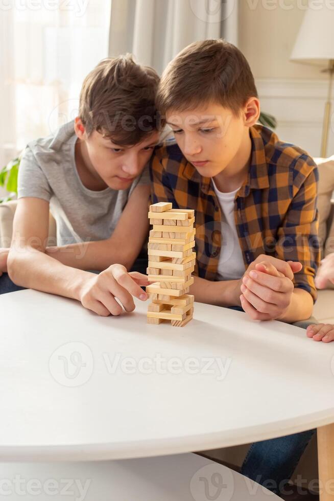A two teen boys are enthusiastically playing a board game made of wooden rectangular blocks photo