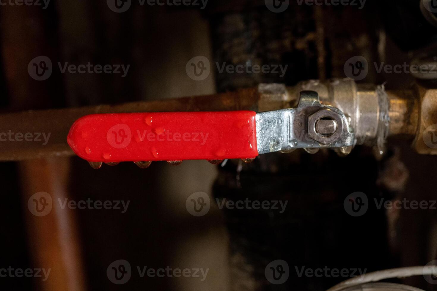 Red lever handle on metal pipe with water droplets in industrial setting photo