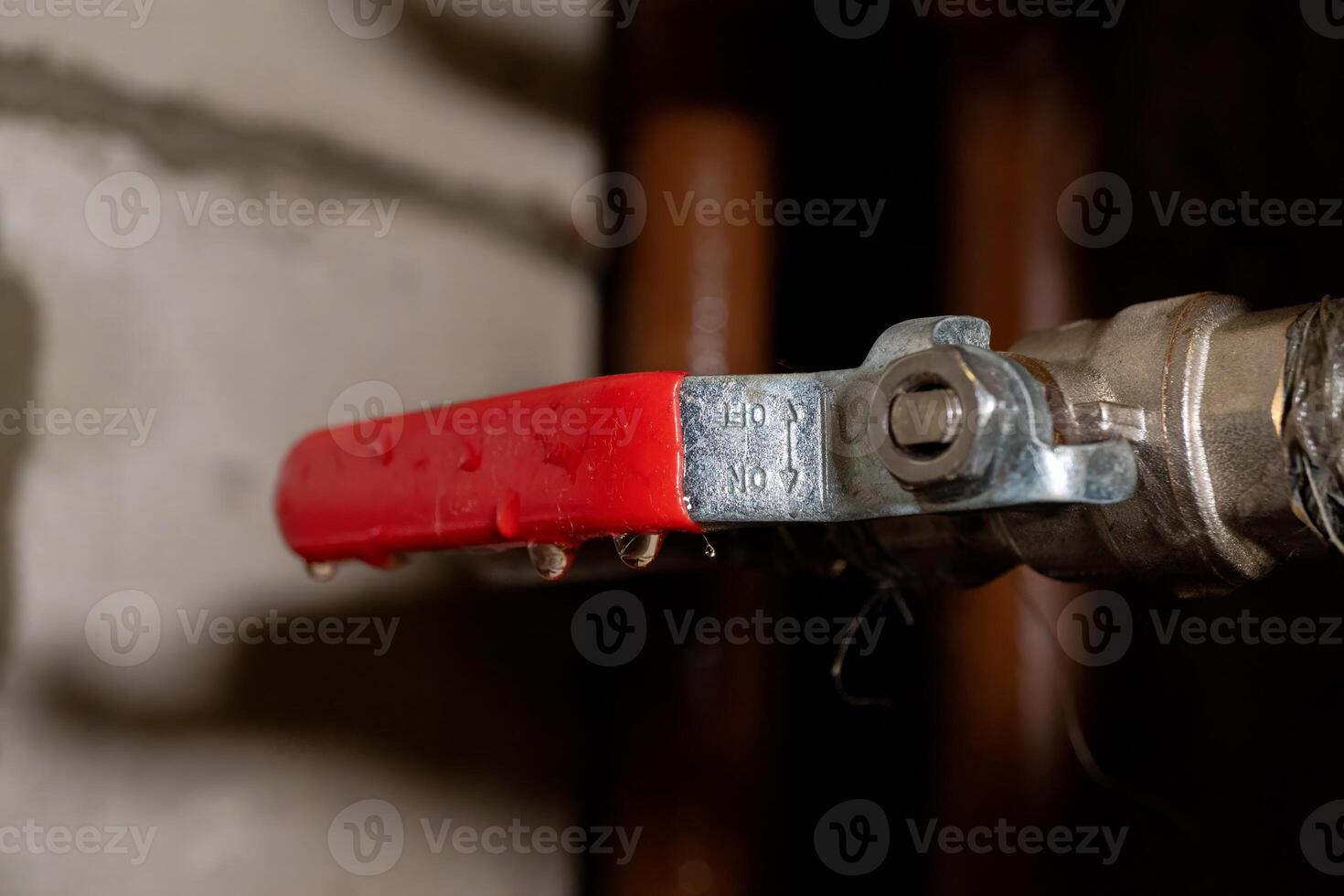 Close-up of red metal valve handle with water droplets on industrial pipe photo