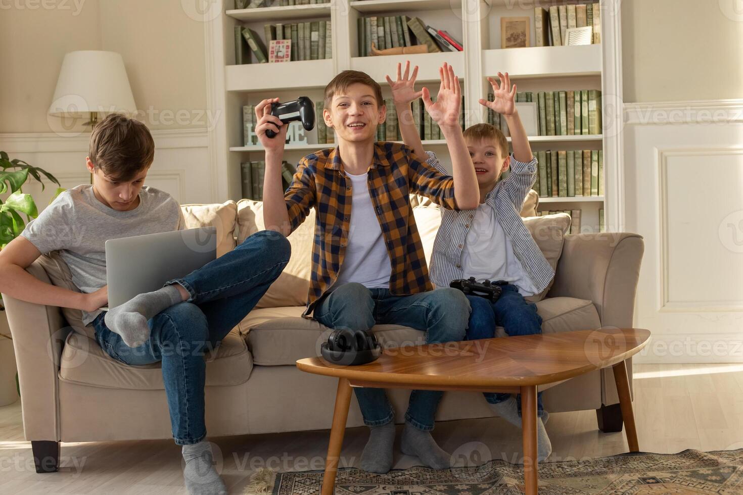 Three brother boys playing computer games on a laptop and games with joysticks photo