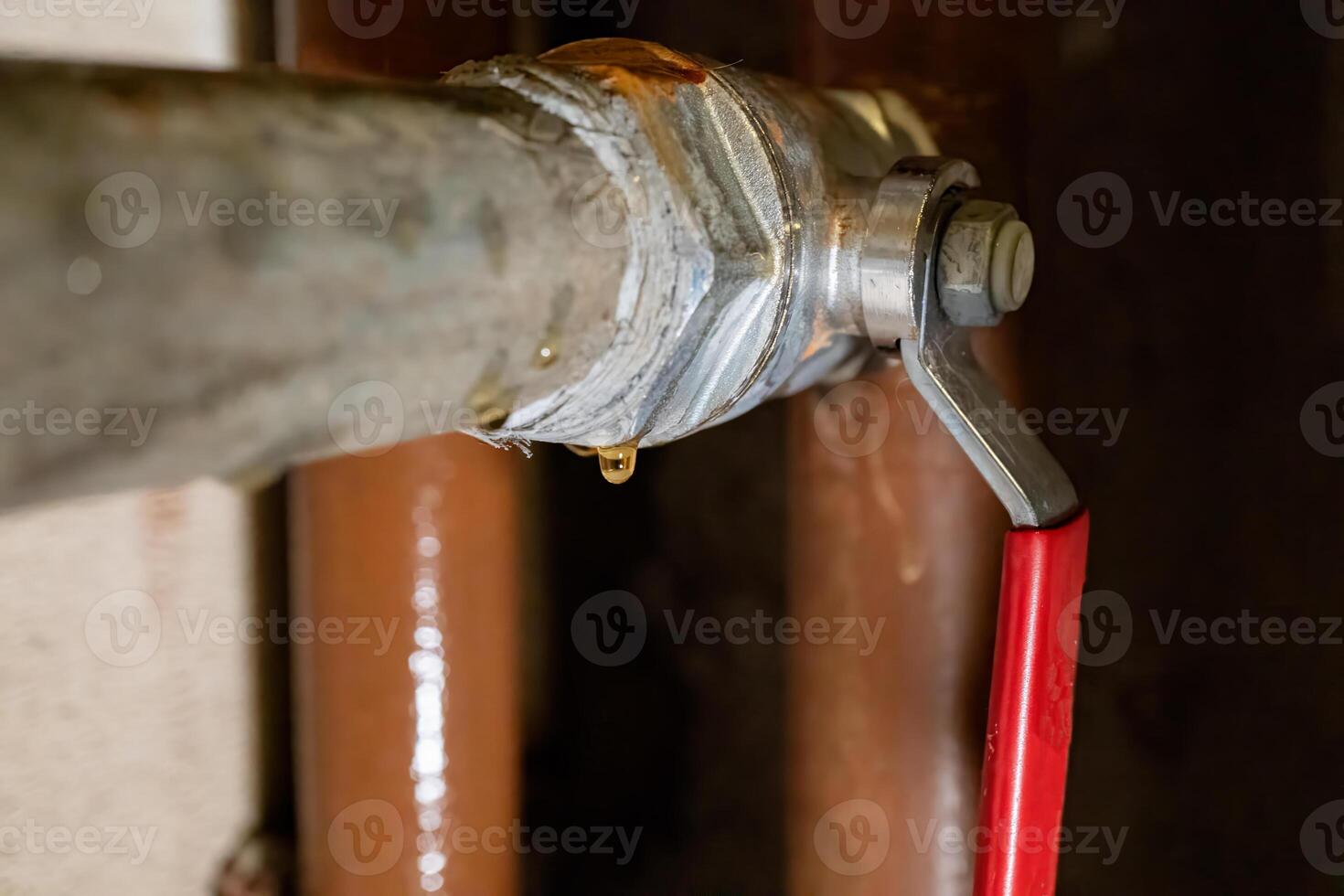 Leaking pipe valve with metal fittings and red handle in need of repair photo