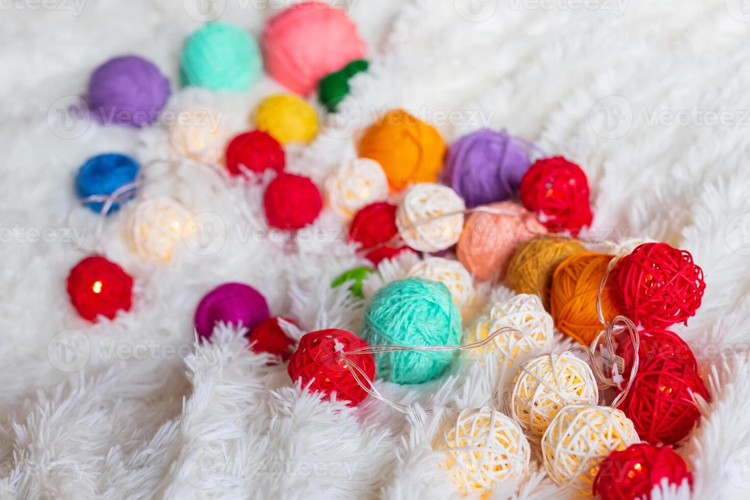 A lot of colorful knitting yarn and a luminous garland in the form of balls lie on fluffy blanket. photo