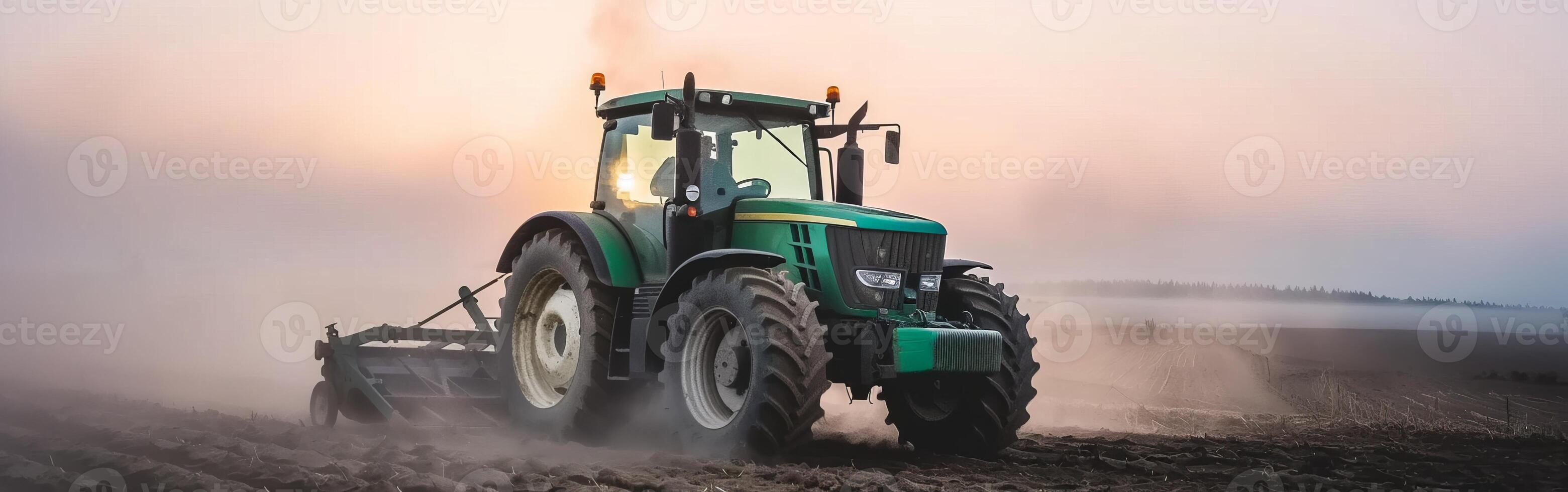 Green tractor plowing a dusty field at sunrise in rural countryside photo