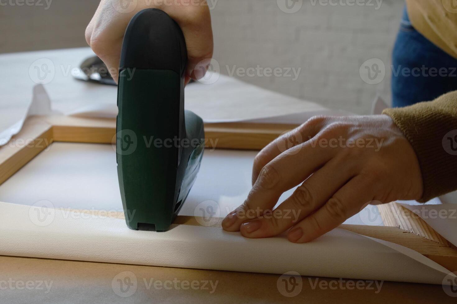 Hands stretching canvas on stretcher bars using staple gun in workshop. Gallery wrap. Print on canvas. photo