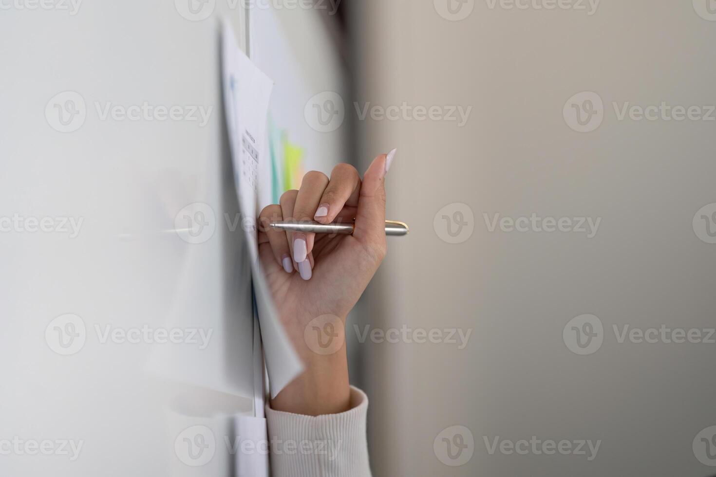 Hand holding a pen against a wall with financial documents, representing analysis and organization. photo