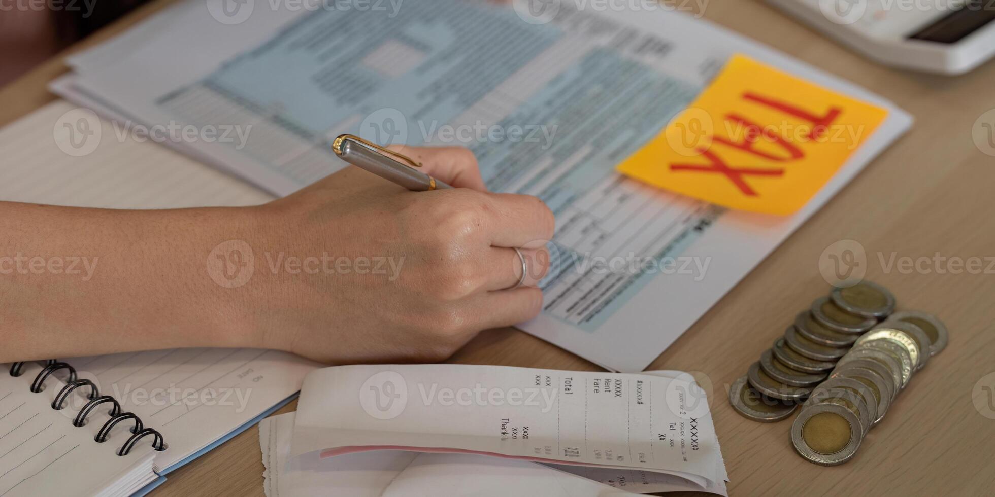 Close-up of woman writing on tax documents with calculator and cash, emphasizing financial organization. photo
