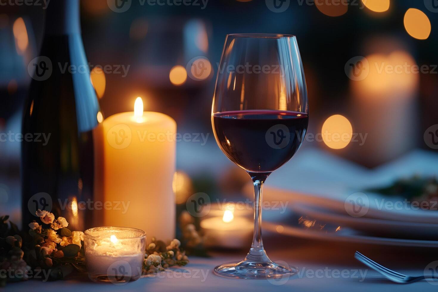 Glass of red wine with candles illuminating romantic dinner table photo