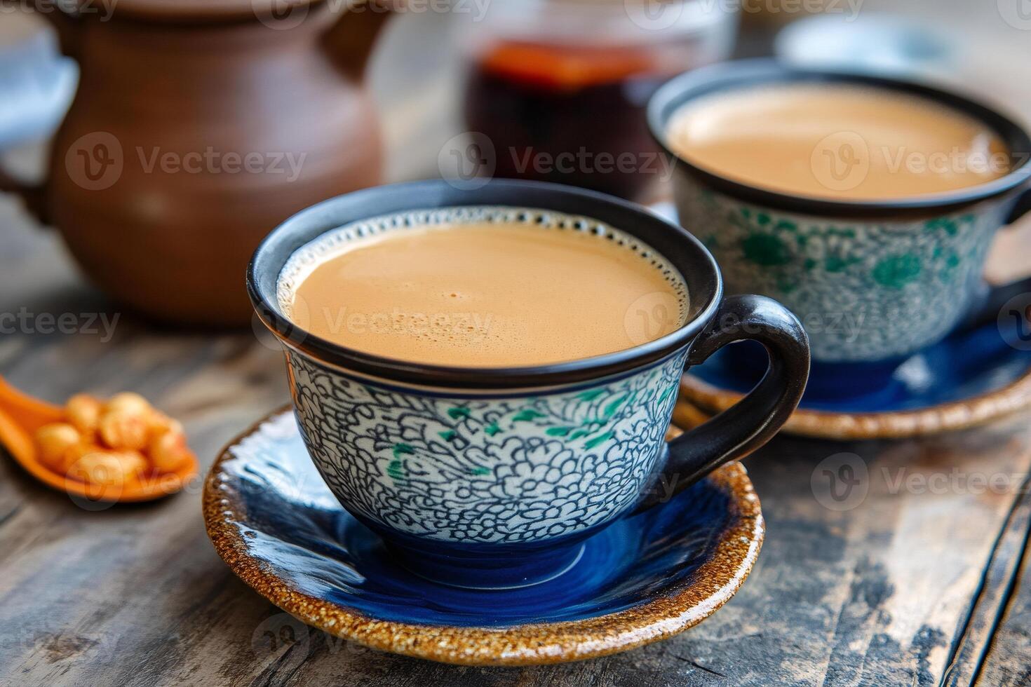 Two cups of masala chai resting on blue saucers with teapot and roasted peanuts on wooden table photo