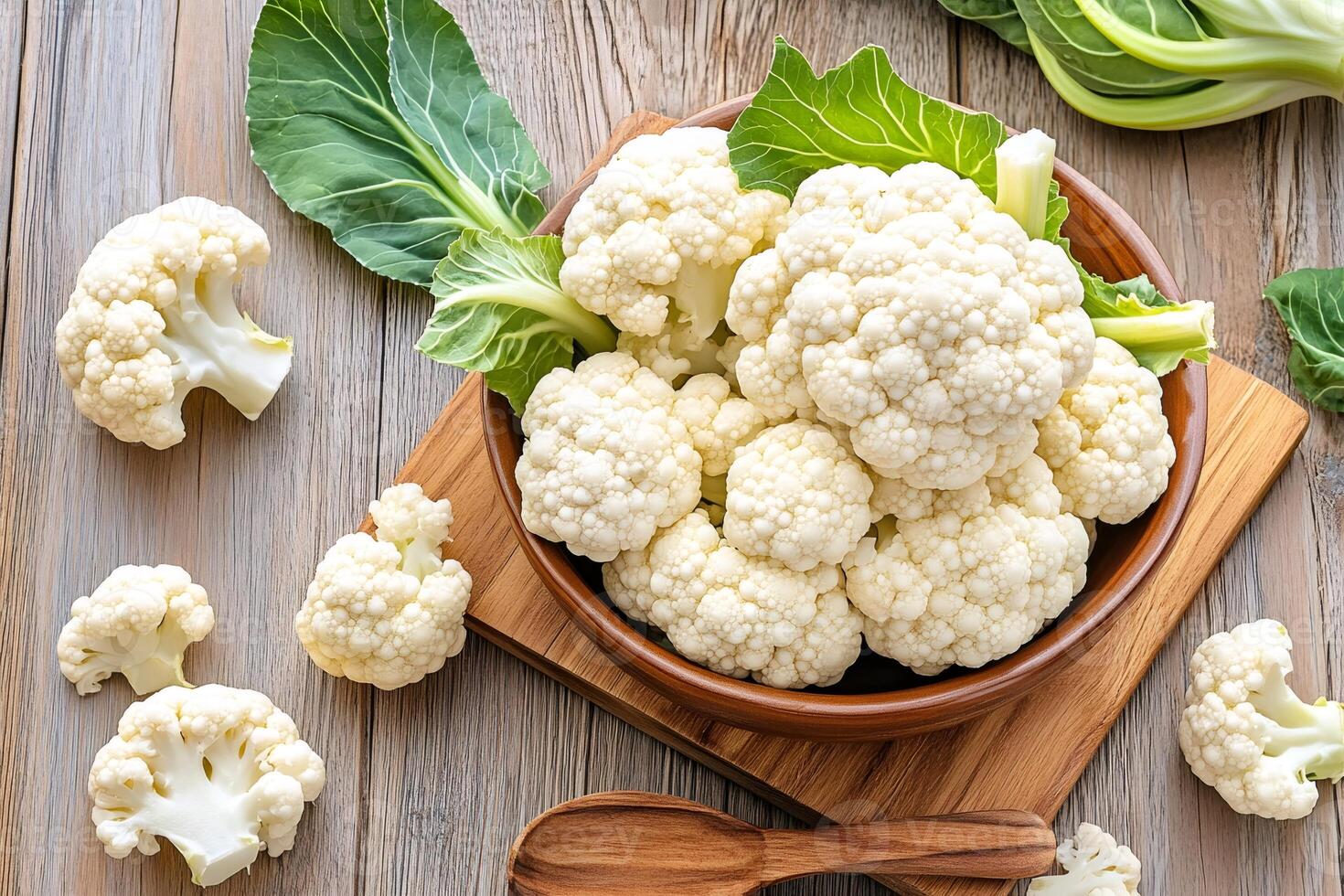 Fresh cauliflower florets in a wooden bowl sitting on a wooden cutting board photo