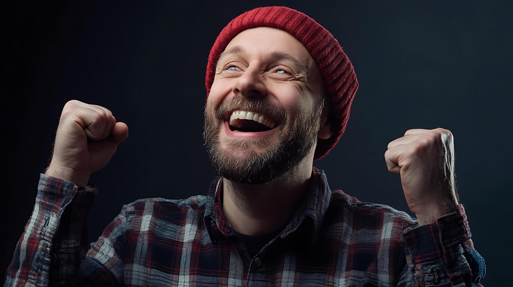 Man Celebrates Success with Joyful Expression Wearing a red beanie he looks upward with a genuine smile and raised fists photo