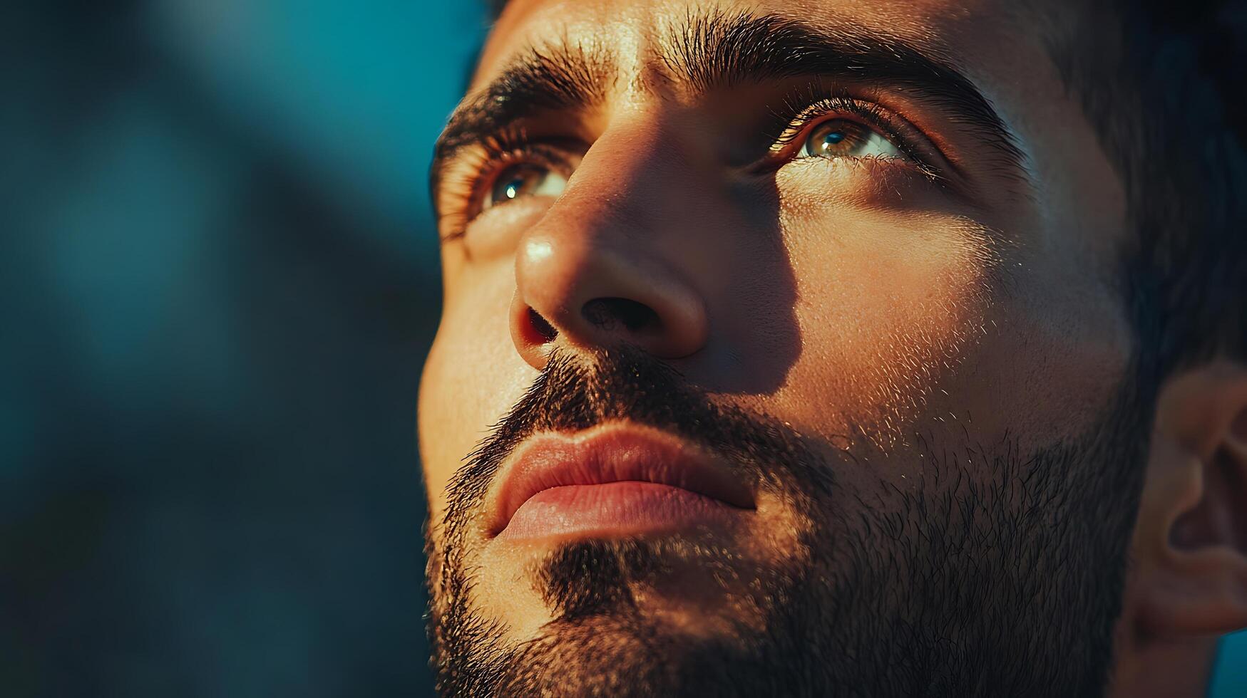 A close up of a man with a beard looking up into the sky A handsome man illuminated by natural light looks hopefully to the heavens photo