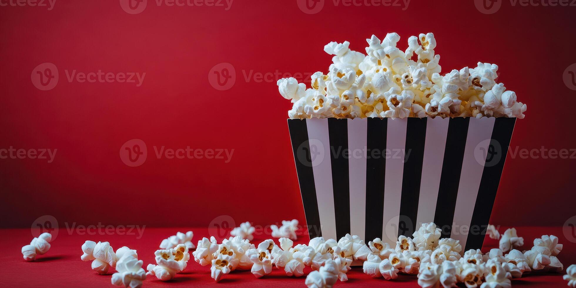 Freshly popped popcorn spilling from a striped box on a red background ideal for movie night photo