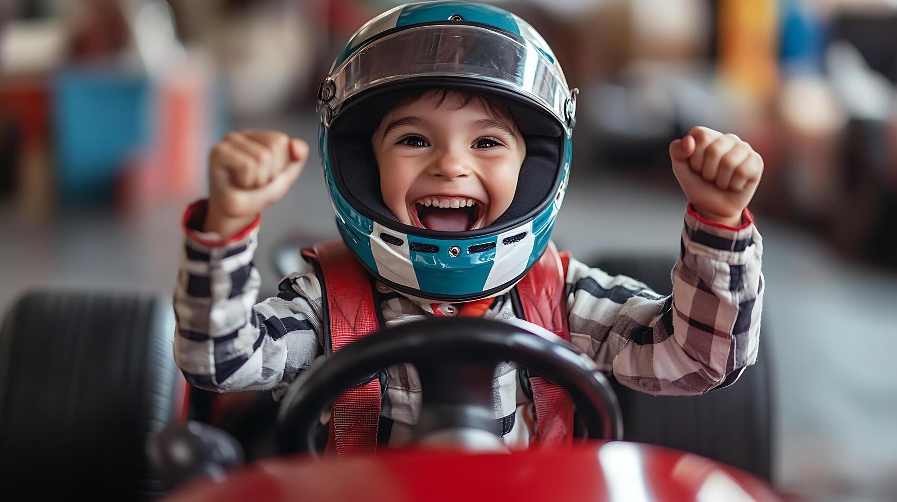 A young boy is racing with a car on a track He wears a helmet and looks happy He is cheering with his hands raised in the air photo