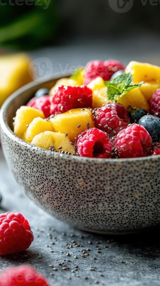Freshly prepared fruit salad with raspberries, blueberries, and pineapple in a textured bowl on a stone surface photo