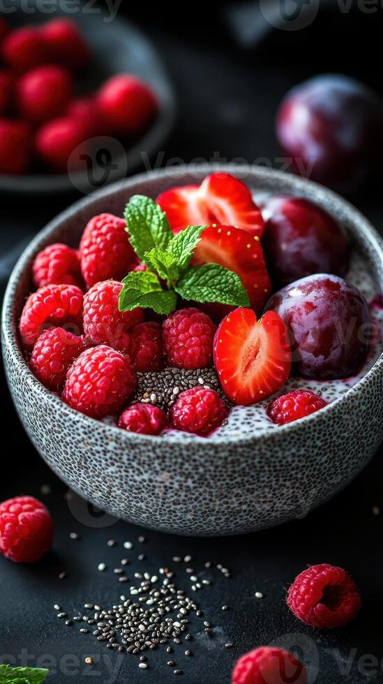 Fresh berries and fruits served in a textured bowl with mint garnish on a dark background photo