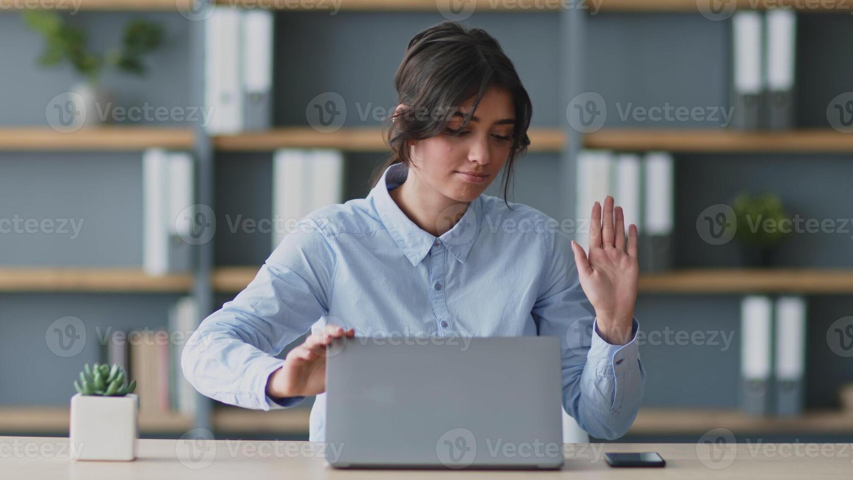 A millennial woman engages in an online lesson while sitting at her desk. She uses a laptop to deliver education remotely and interacts with her students in a modern home setting. photo