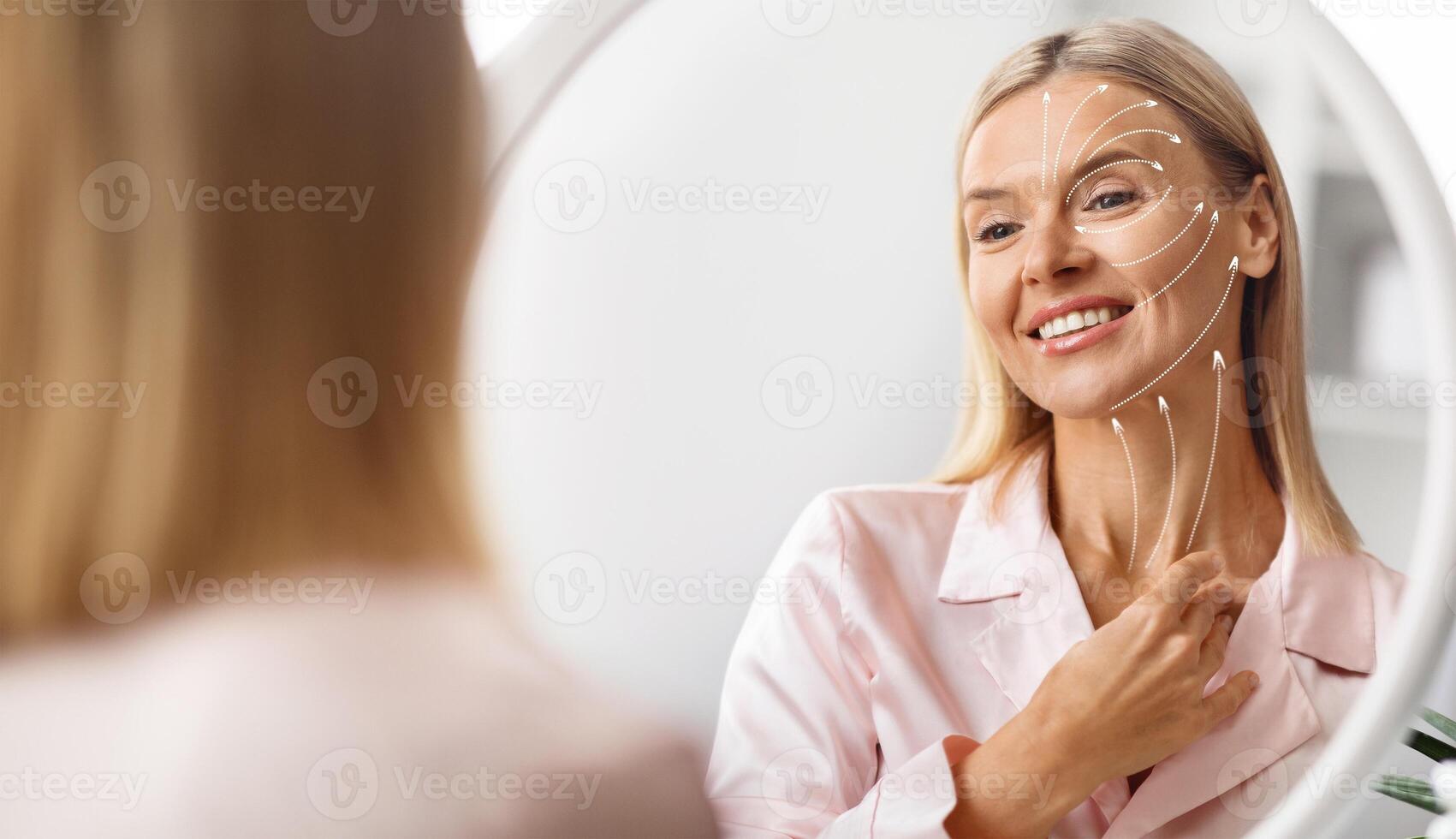Middle aged woman smiles at her reflection while pampering herself with a facial massage at home. She focuses on anti-aging techniques, enjoying a moment of self-care and relaxation. photo