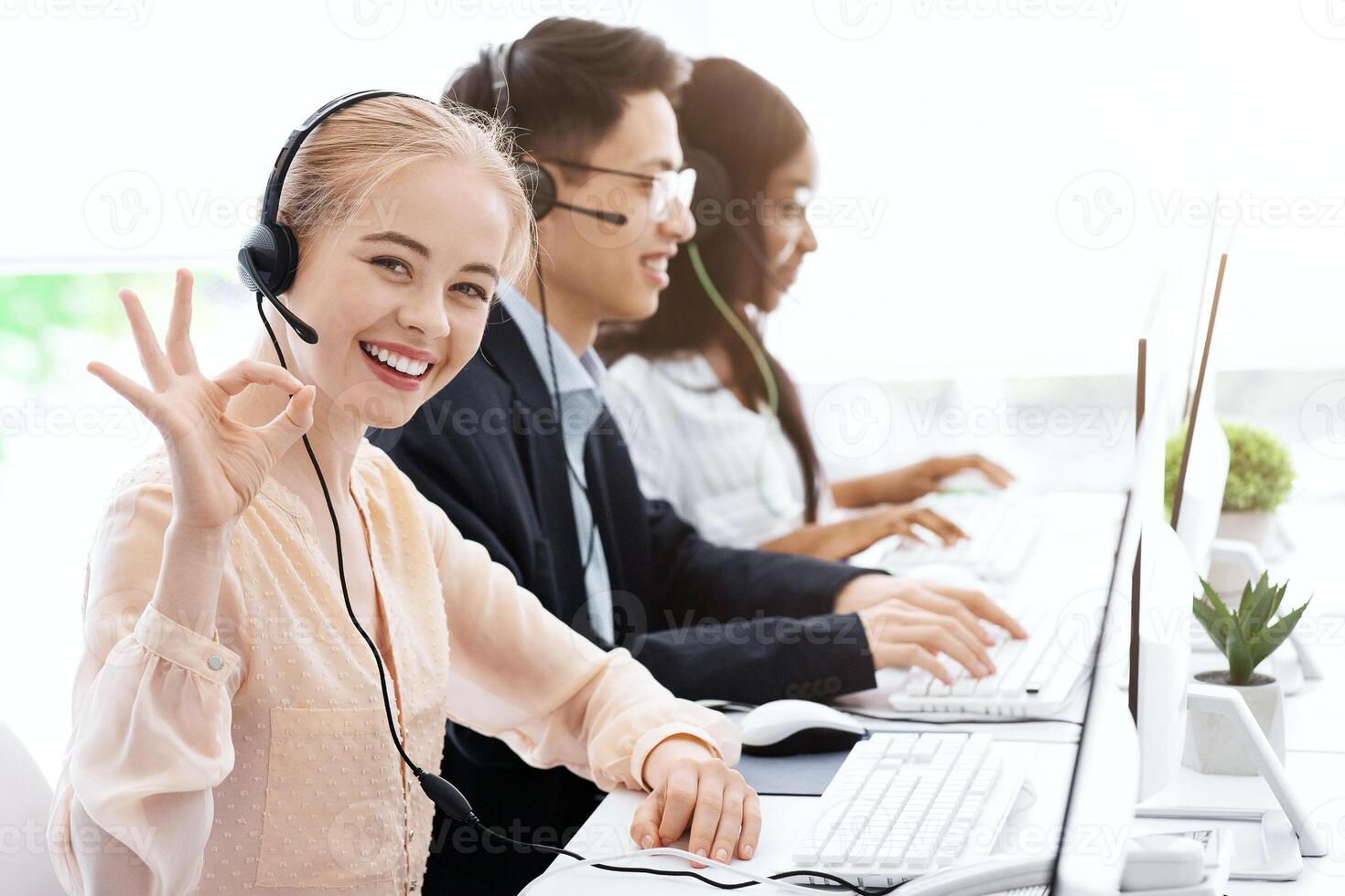 Customer service executive showing OK gesture and her colleagues working at call centre photo