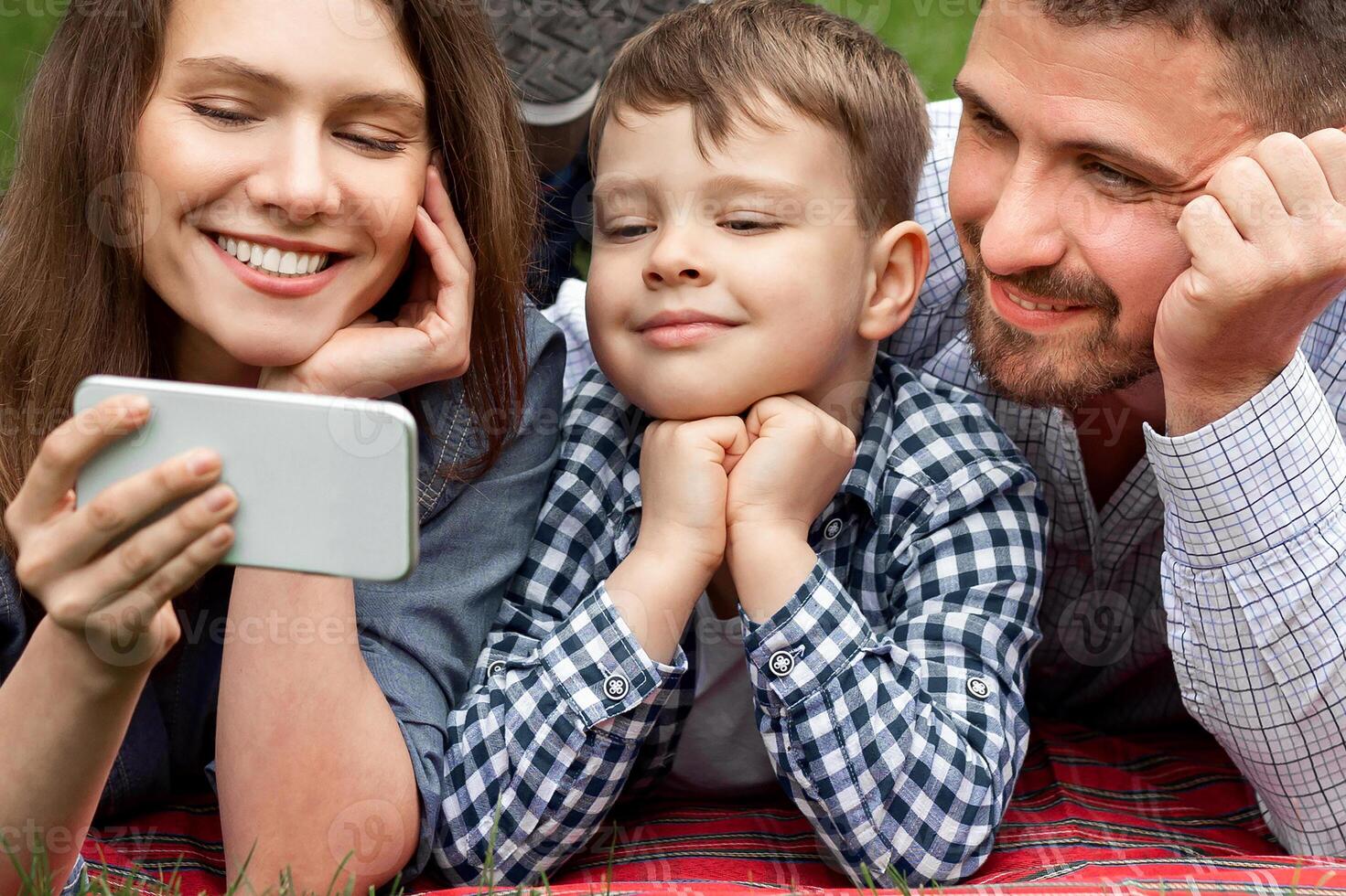Happy family with smartphone watching entertainment on picnic in park, panorama photo