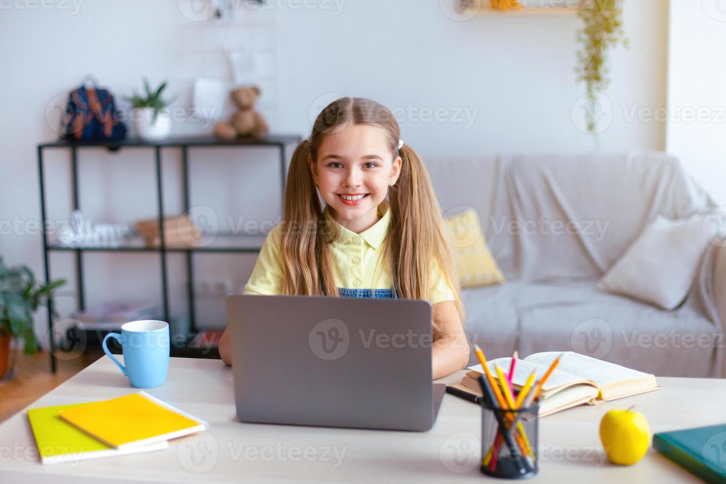 Distance Education. Smiling girl sitting at table, using laptop computer and looking at camera, watching tutorial, virtual lecture or lesson, studying online at home. E-learning And Knowledge photo