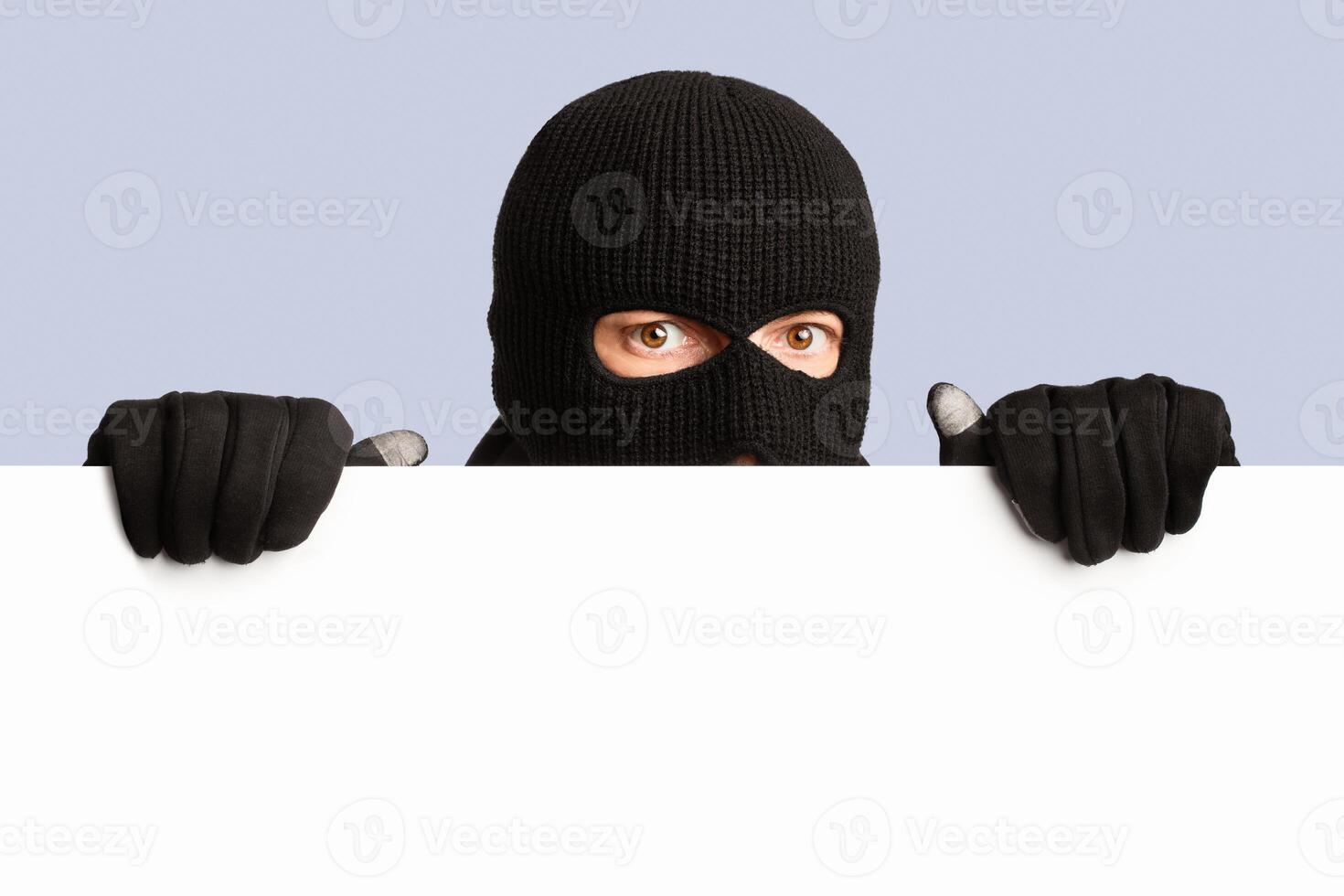 Closeup portrait of disguised looter peeping out white blank advert billboard, isolated over white studio background photo