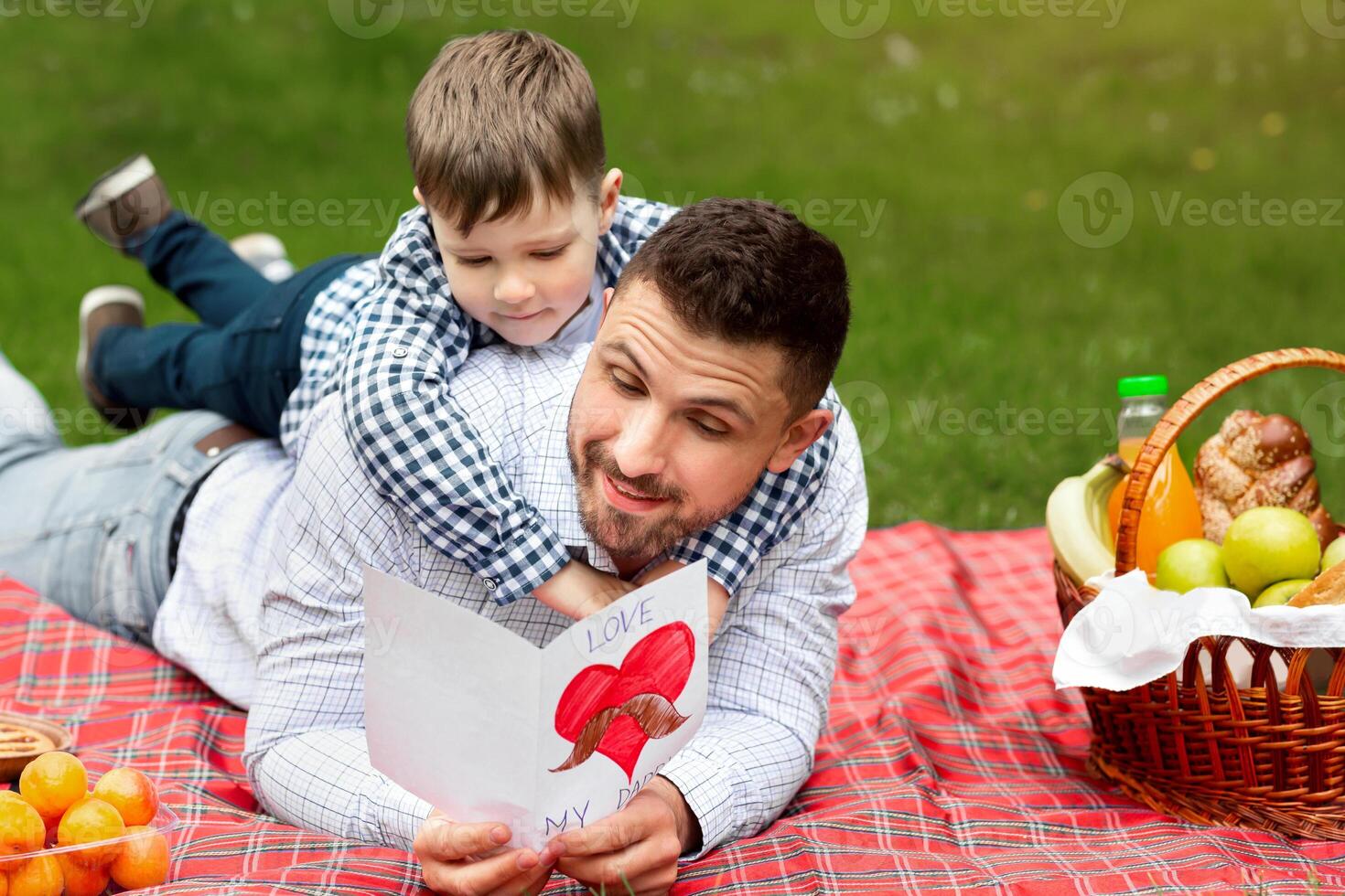 Father Day celebration. Happy dad reading his son's greeting card on picnic in public park photo
