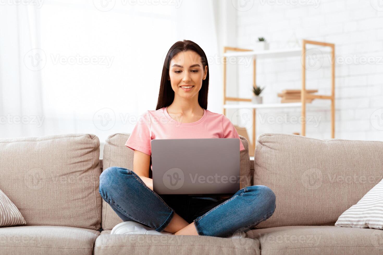 Lifestyle Concept. Happy smiling woman using laptop sitting on sofa in living room at home, watching funny , reading news. Student learning language, calling or working online on freelance photo