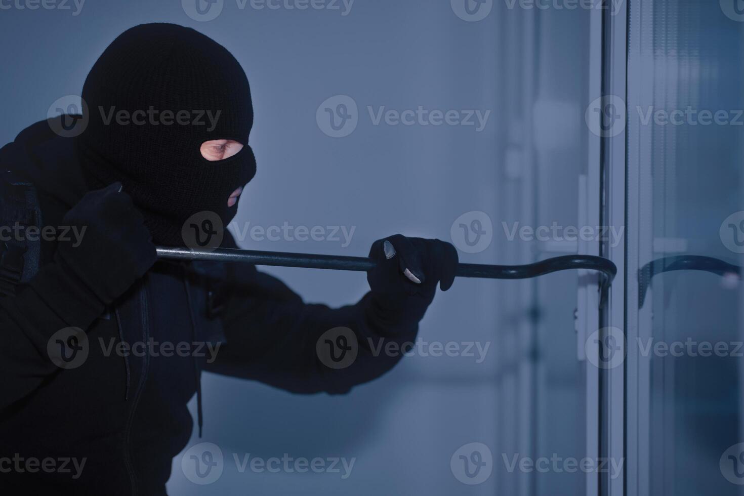 Home Security Concept. Burglar in Action Trying To Break Into the House Using Crowbar, Side View photo