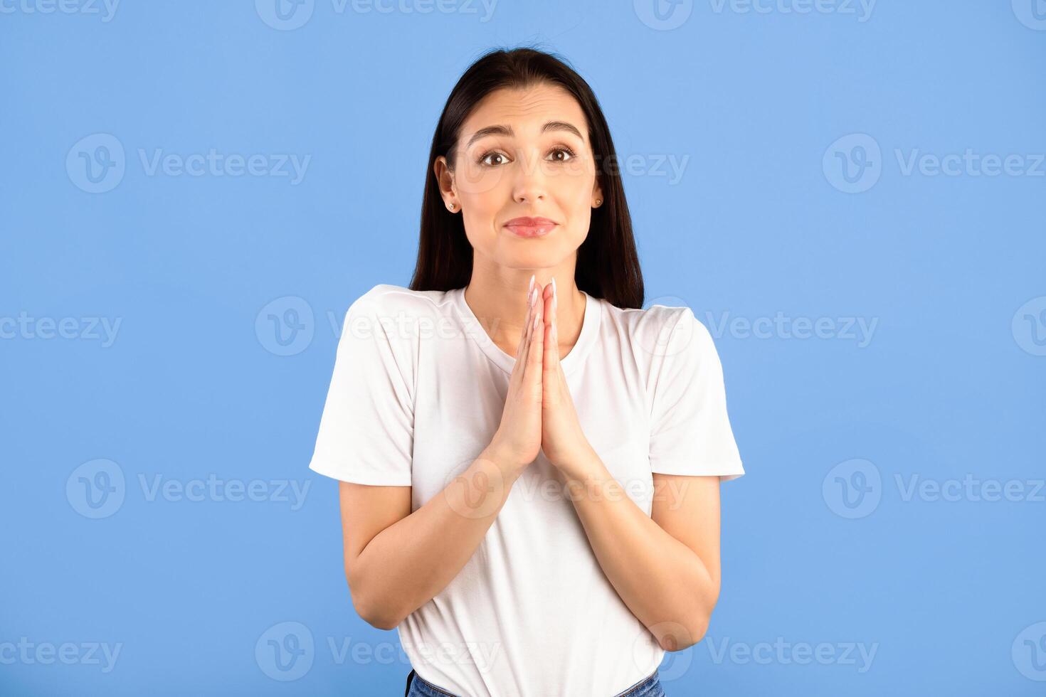 Pleading Concept. Portrait of pretty woman keeping palms together with apologizing expression asking to do her a favour. Hopeful young female model making request, hoping for mercy, dreaming photo