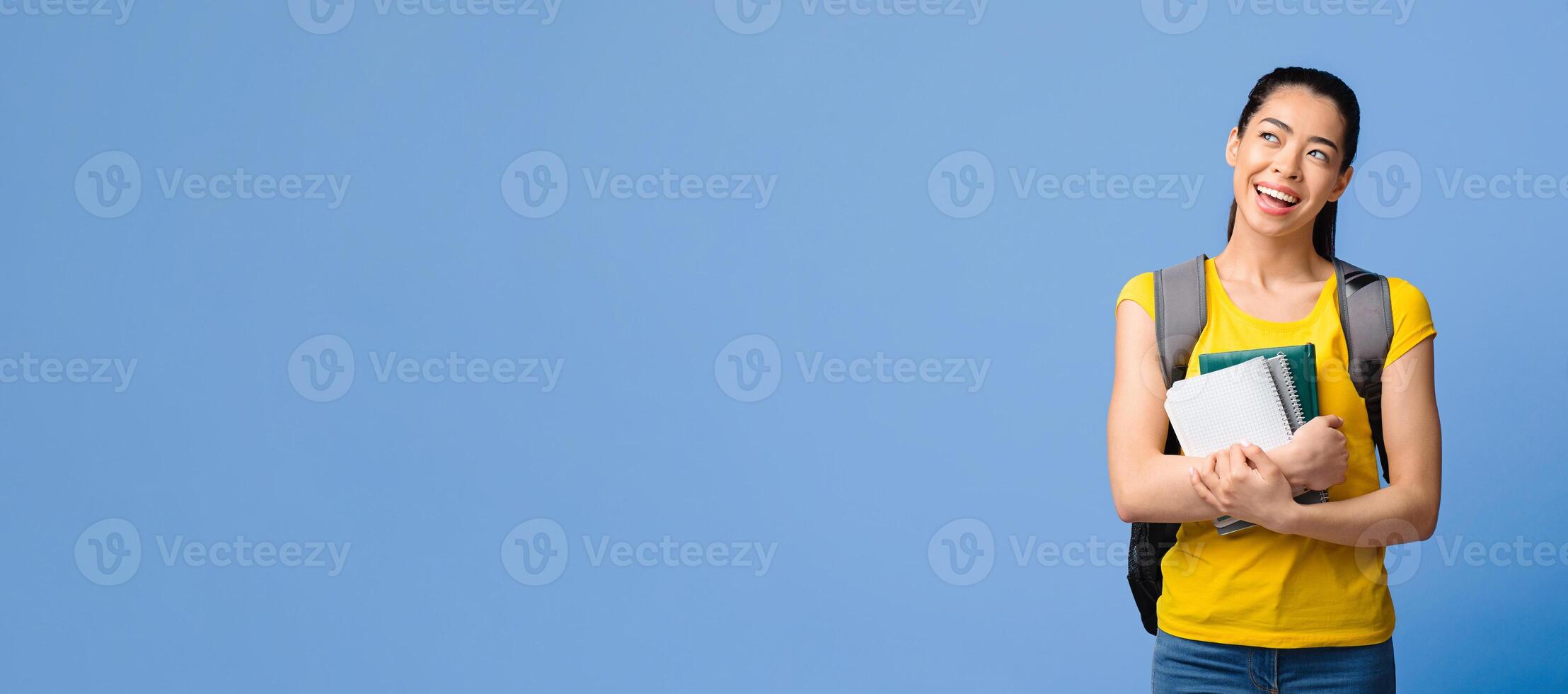 Dreamy korean female college student with backpack and workbooks looking away at copy space over purple studio background, thinking about education program offer and study abroad, copy space photo