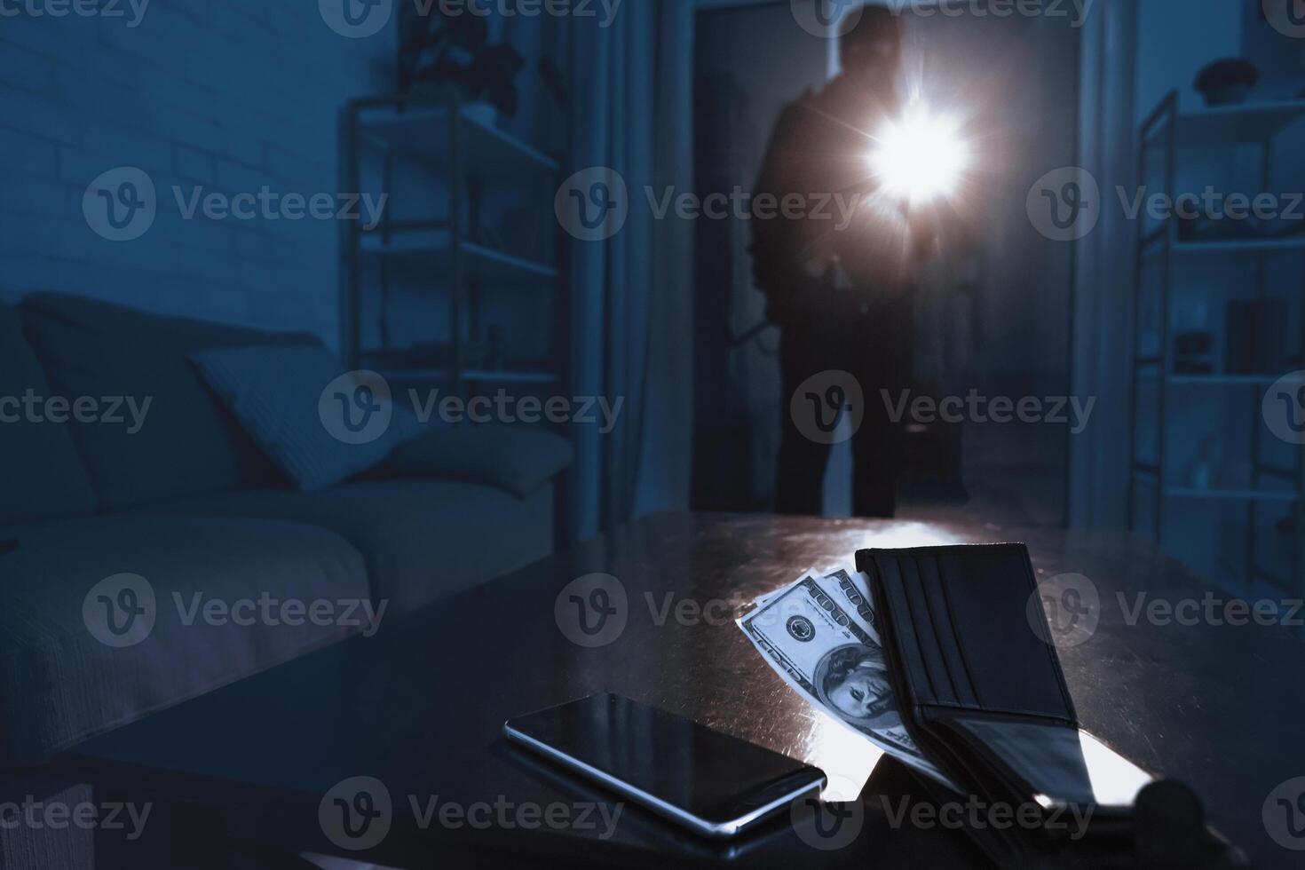 Burglary Concept. Robber breaking into modern apartment, using flashlight, cash and cell phone lying on the table photo