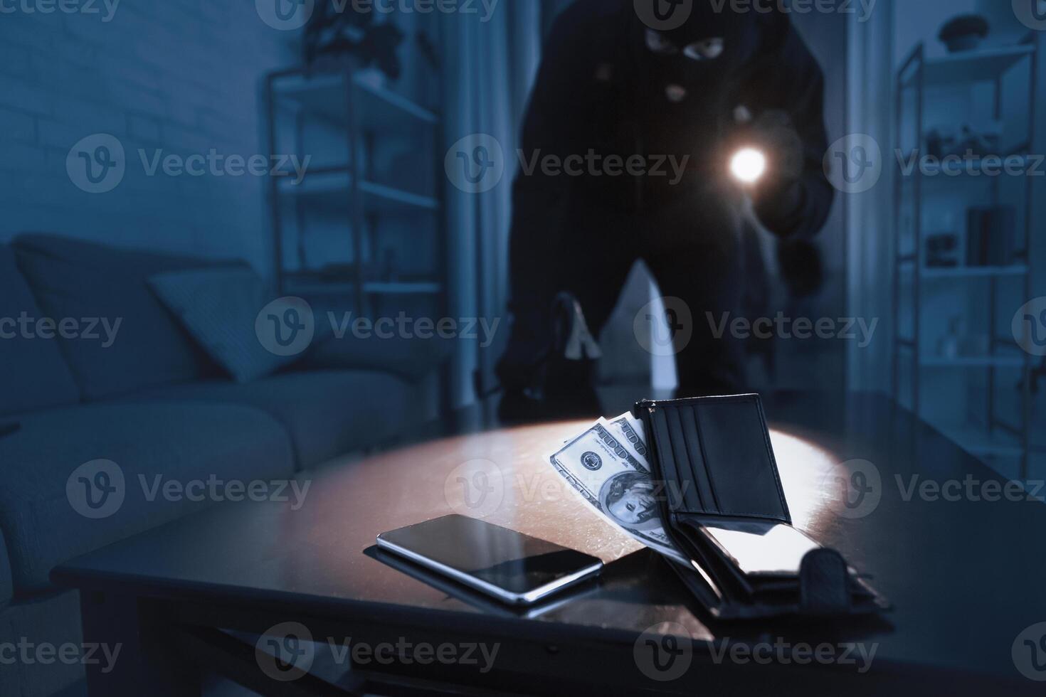 Home Invasion. Masked robber breaking into home at night through back door, using flashlight on cash and smart phone photo