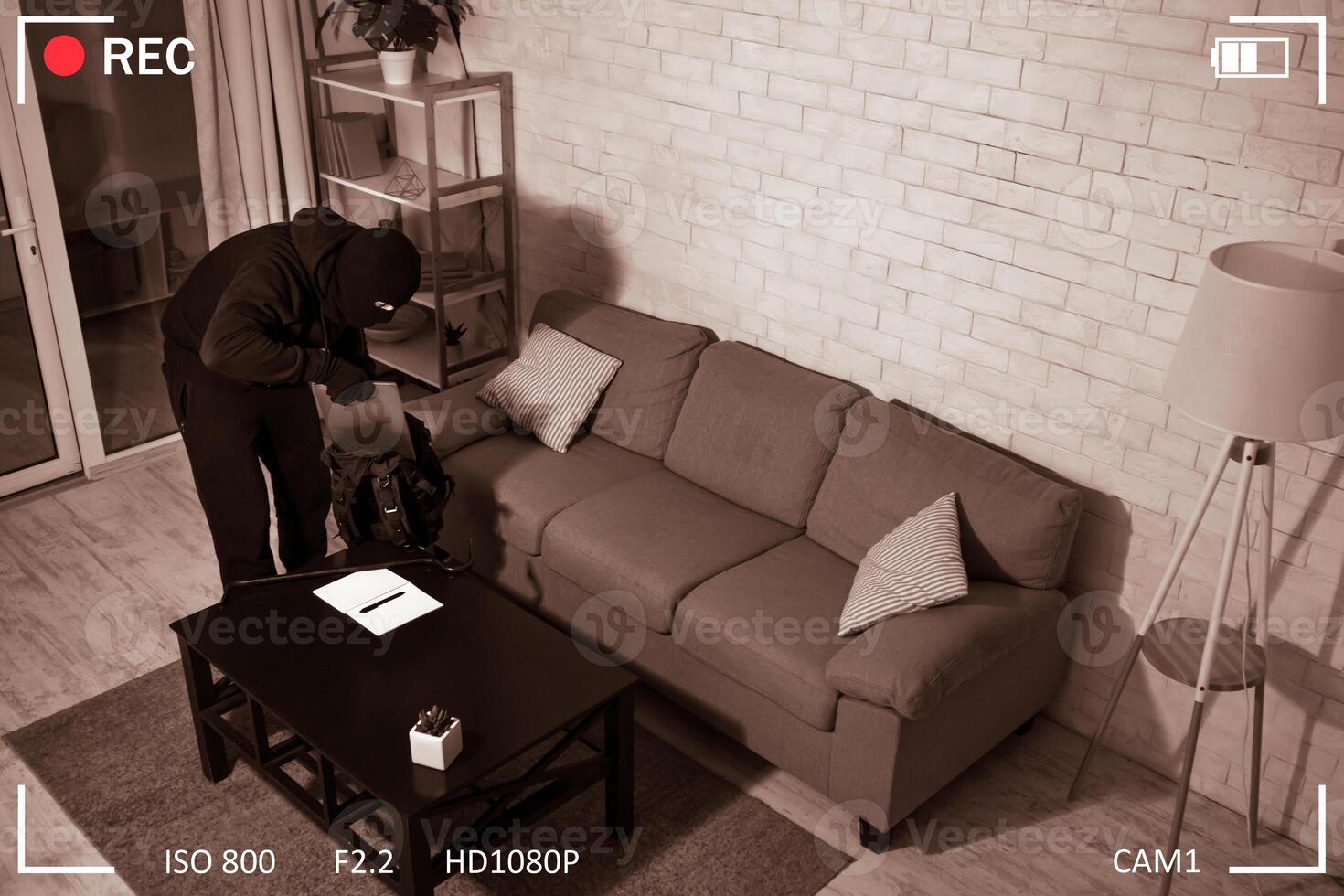 Supervision Concept. Masked looter stealing pc, putting it in his backpack in the dark, view from above, black and white photo
