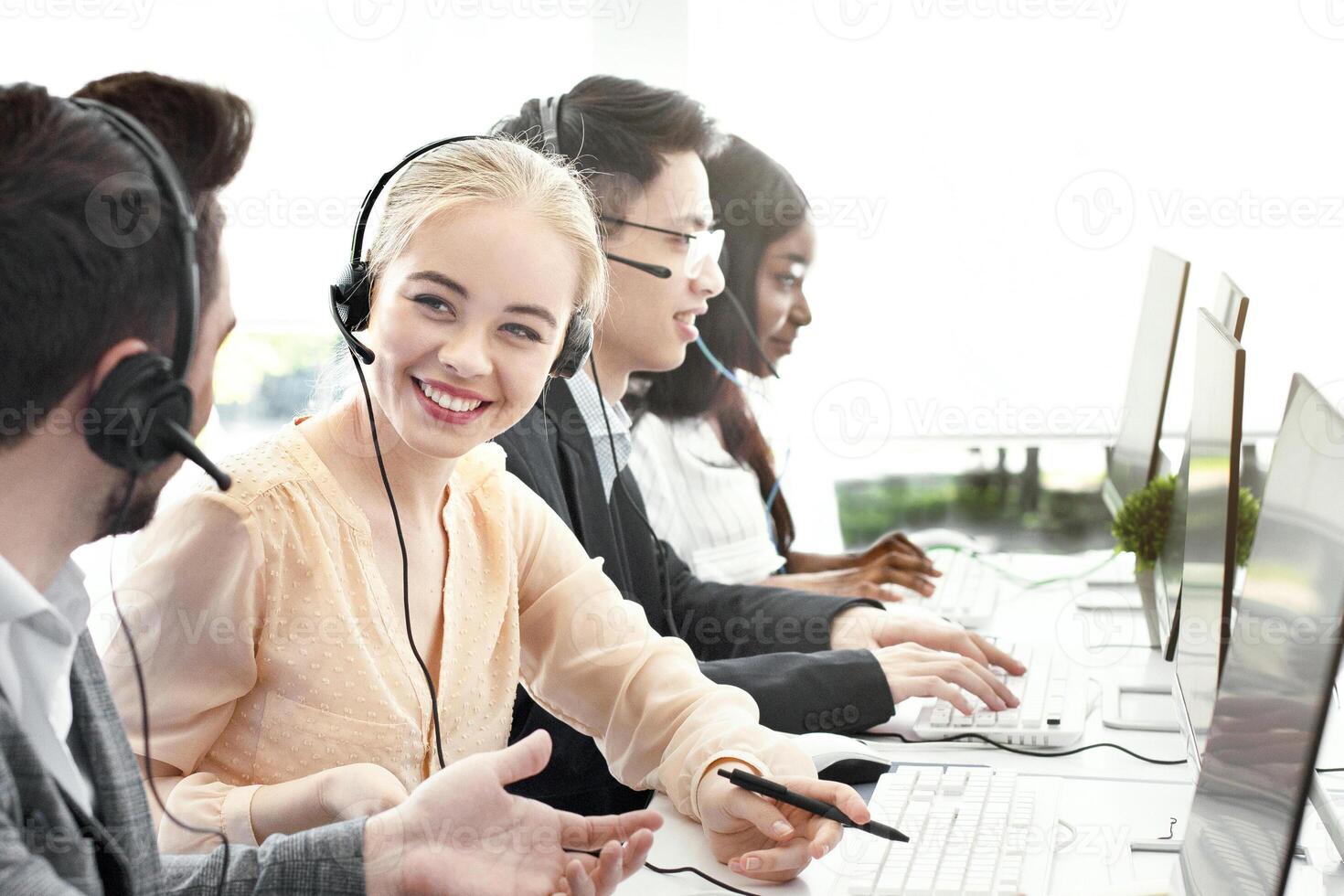 Smiling customer support workers communicating to solve client's problem together at call centre office. Positive hotline operators with headsets having conversation at workplace photo