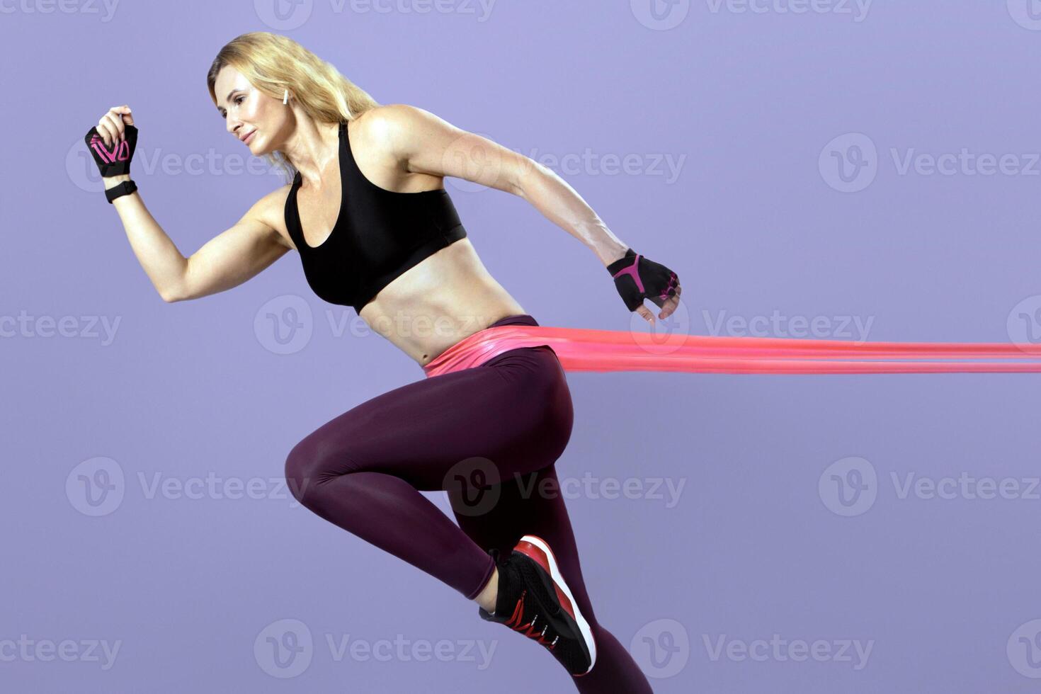 Weight loss, pilates, fitness equipment and active workout. Middle aged muscular lady in sportswear runs and does exercise with elastic band, isolated on purple background, profile, panorama photo