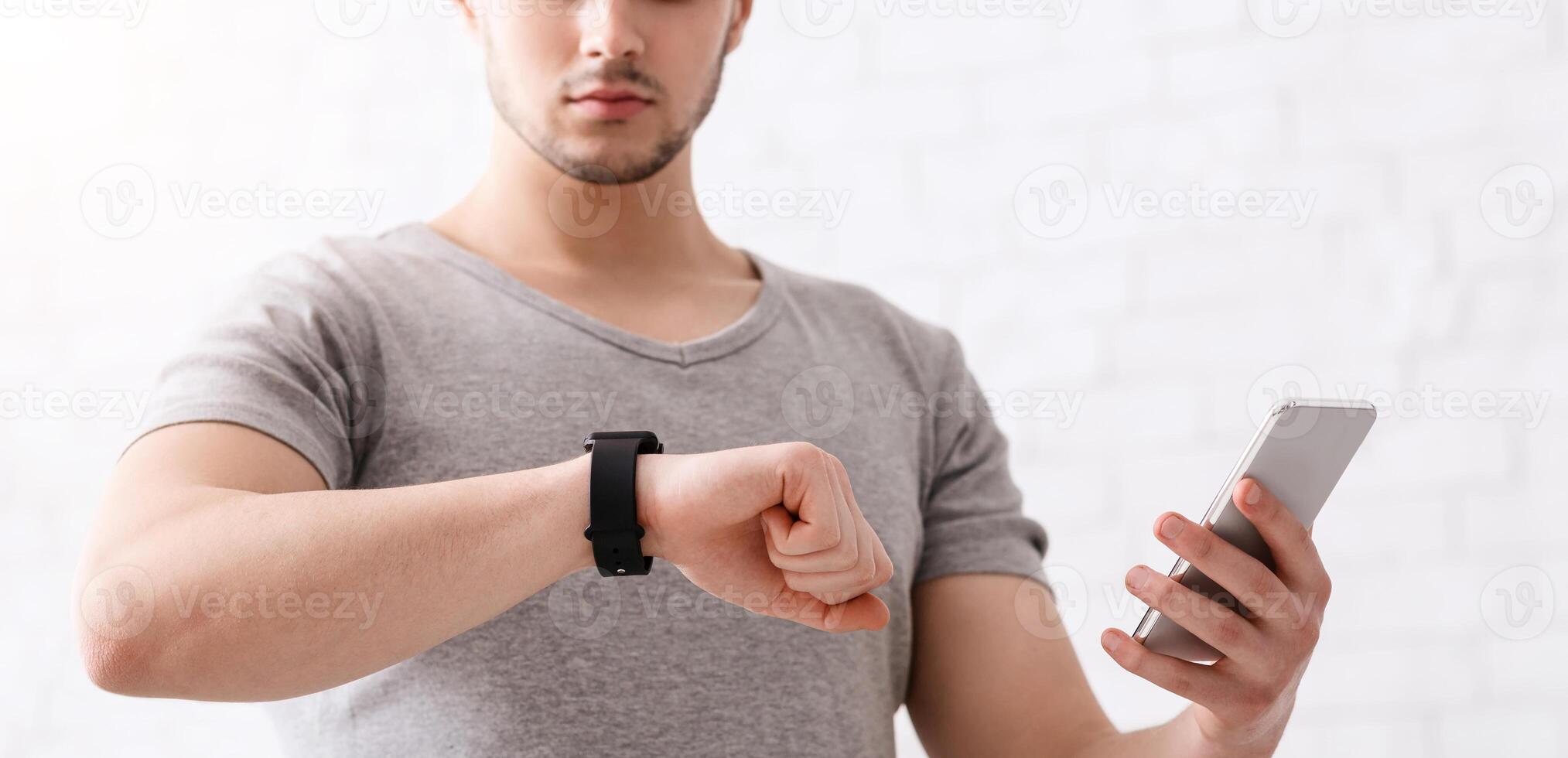 Modern technologies for sport. Guy with fitness tracker on his hand and smartphone, checks activity at light background at home photo