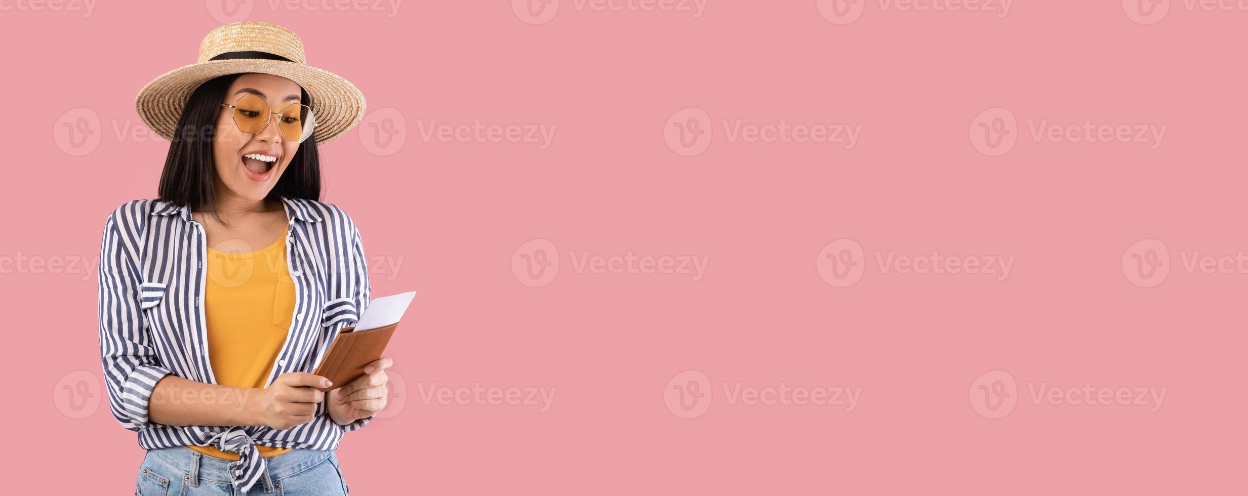 Finally Vacation. Portrait Of Excited Asian Woman Holding And Looking At Her Passport And Plane Boarding Pass Tickets, Ready For Summer Trip, Wearing Straw Hat And Sunglasses, Pink Studio Background photo