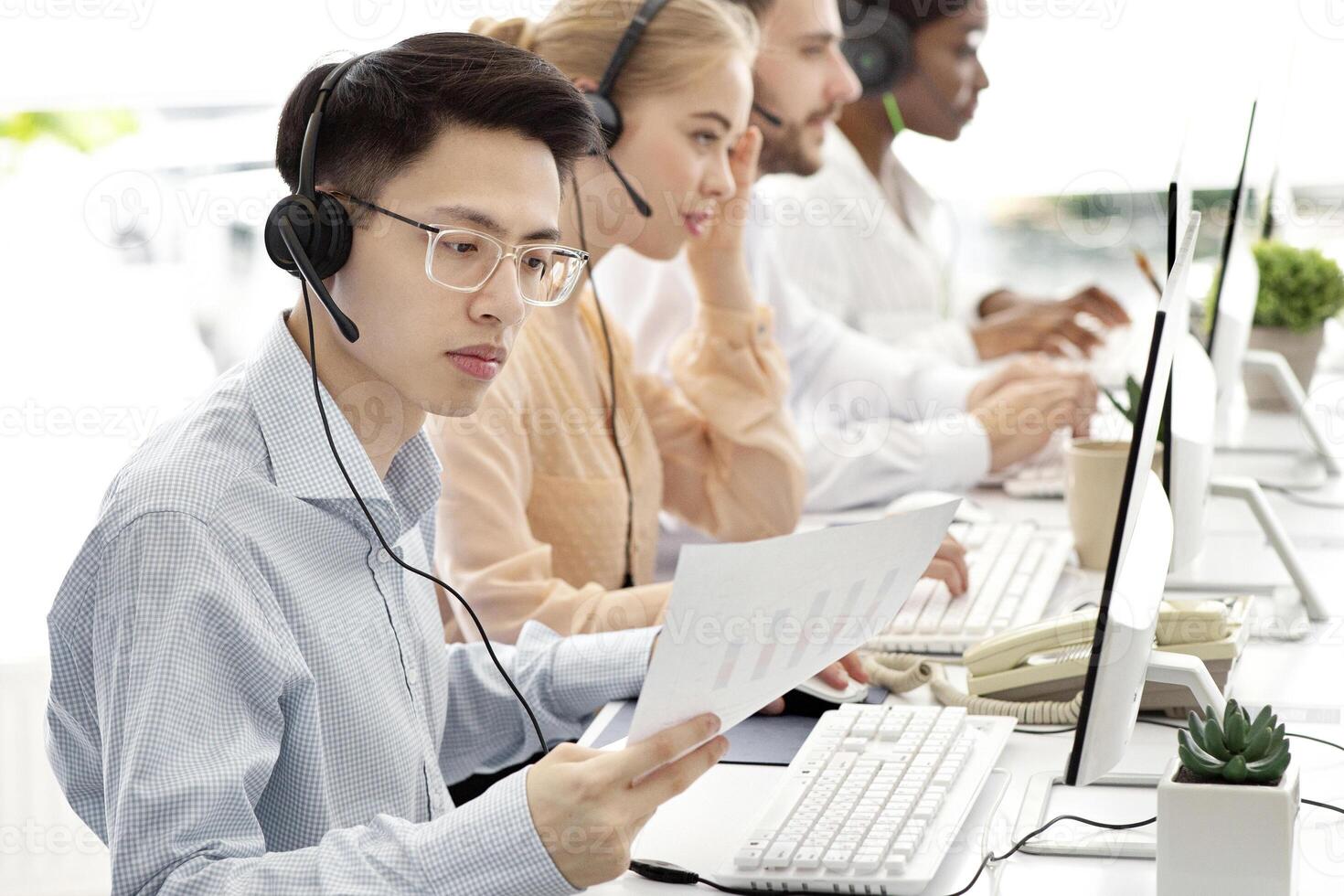 Asian hotline operator working with documents, providing technical support services to clients, free space. Call centre representatives talking to customers or selling goods online photo