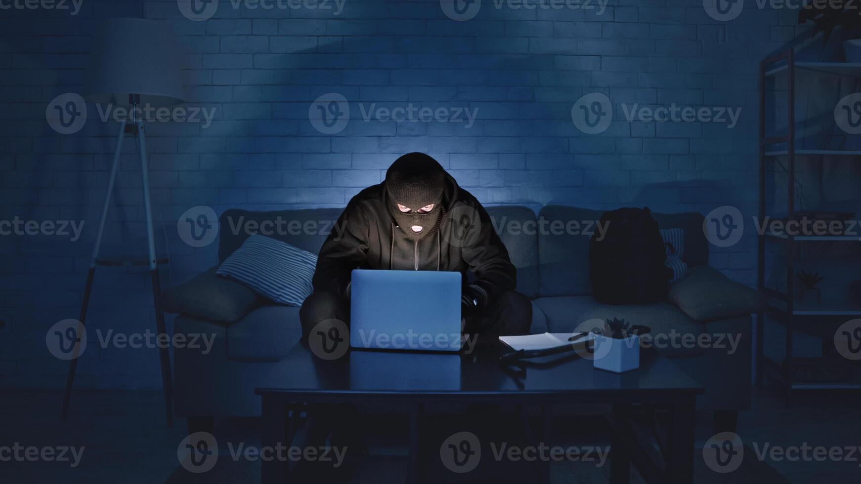 Cybercrime and Spying Concept. Masked criminal using computer at night, making cyberattack, breaking the law photo