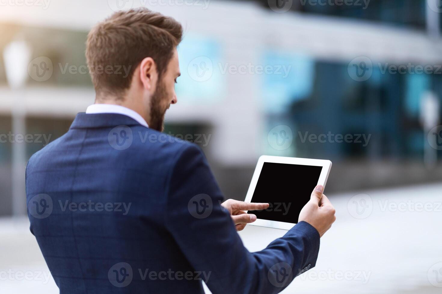 Business executive holding tablet computer with blank screen near office building, mockup for your design photo