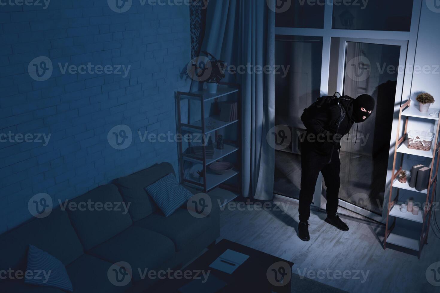 Life After Lockdown. Disguised stealthy robber entering apartment in the dark, holding crowbar, high angle view photo